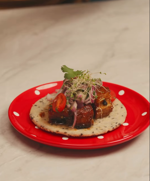 Arepa con semillas de sésamo negro, panceta con salsa de tamarindo, cebolla morada, tomate y brotes
